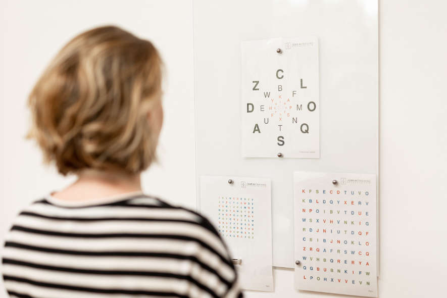 Genrebild für Neuroathletisches Training - Frau schaut auf eine Tafel mit mehreren Blättern, auf denen Buchstaben zu sehen sind. 